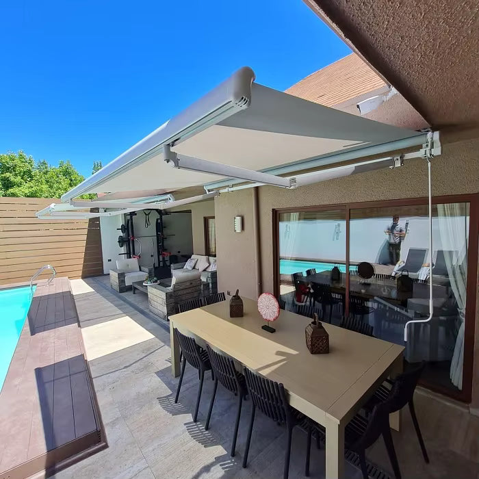 Toldo proyectante gris claro dando sombra a una terraza con piscina y comedor exterior