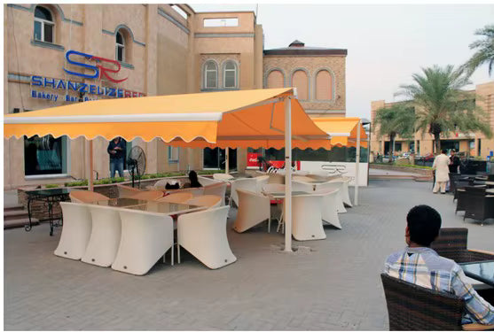 Toldo proyectante naranjo instalado en la terraza de una cafeteria con mesas exteriores