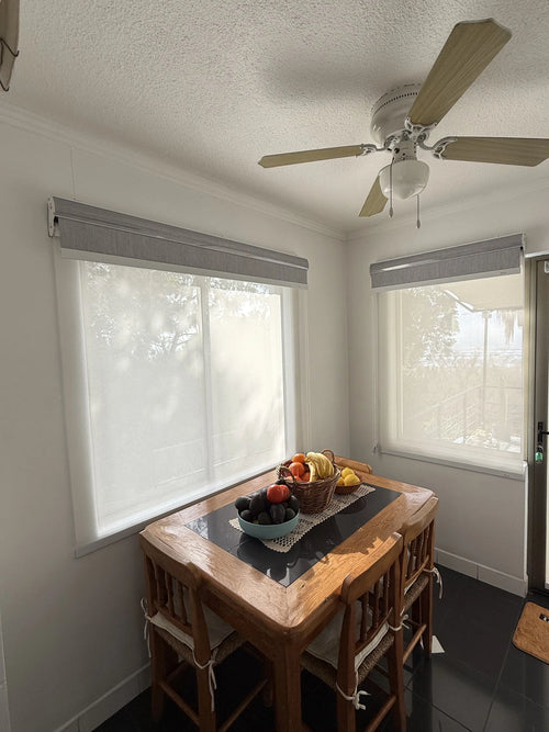 Cortinas roller dobles con tela sunscreen blanca instaladas en ventanas de comedor